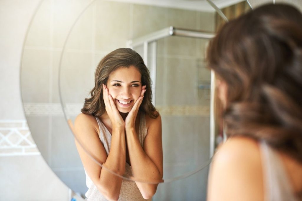 Woman smiling at her reflection in a mirror after a periodontal exam at South Florida Smile Spa in Pompano Beach