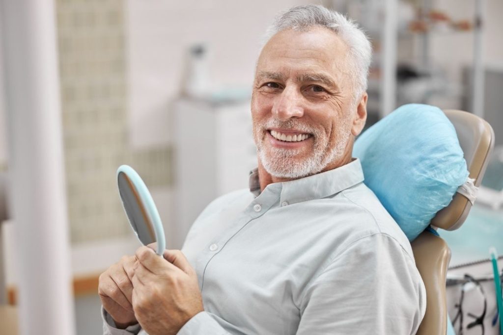 Patient checking his gums in a hand mirror after a gum disease diagnosis in Pompano Beach, FL