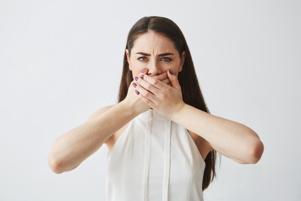 Woman covering her mouth, embarrassed by chronic bad breath (halitosis)