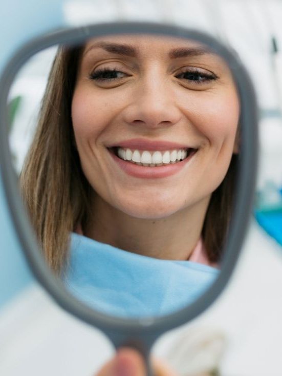 Patient smiling into a handheld mirror in the dental chair
