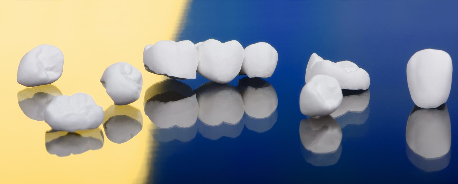 Zirconia dental crowns and a three-unit bridge arranged on a gold and navy background, illustrating dental crown materials.